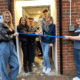 A picture of our Youth Panel smiling and laughing while they cut a ribbon in front of our new home on 64 London Road