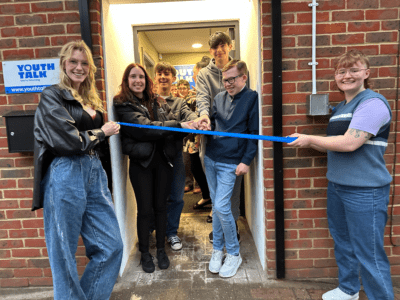 A picture of our Youth Panel smiling and laughing while they cut a ribbon in front of our new home on 64 London Road