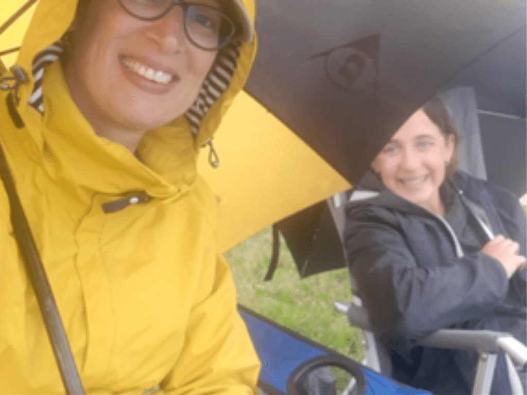 A selfie of Liz Redway in a raincoat and her daughter smiling in a camping chair.