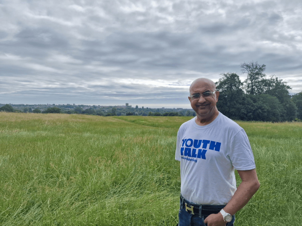 Nashir wearing a Youth Talk t-shirt and smiling in a field during his 13km walk in June.